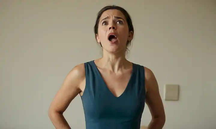 He aquí una respuesta: Una mujer de pie derecho con hombros relajado, pies de ancho de hombro, manos sobre caderas, ojos mirando hacia adelante, expresión facial neutral, y boca ligeramente abierta como si estuviera a punto de bostezar