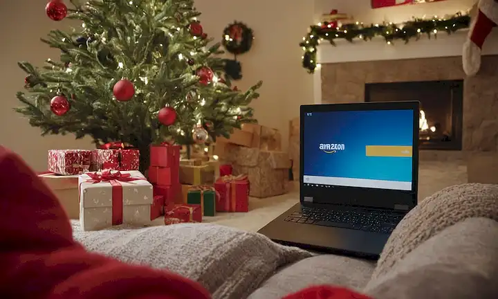 Una persona que compra en línea en un portátil, rodeado de paquetes de Amazon, con una cara sonriente, con una tarjeta de crédito, y con un suéter festivo, en medio de un salón desordenado pero organizado, con una TV jugando en el fondo, mostrando un banner de descuento, cerca de un estante lleno de libros y electrónica, con una flecha roja apuntando a la pantalla, y un toque sutil de un árbol de Navidad en la esquina