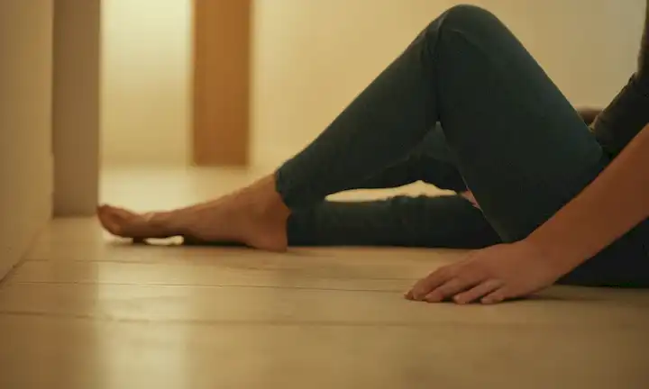 Una persona sentada o acostada en un suelo, un fondo borroso, un enfoque en la pelvis y piernas, iluminación suave, tonos cálidos, sombras mínimas, texturas sutiles, no colores audaces